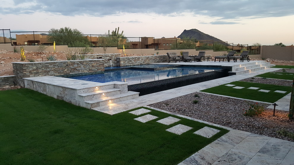 Exemple d'une grande piscine à débordement et arrière tendance sur mesure avec des pavés en pierre naturelle et un point d'eau.