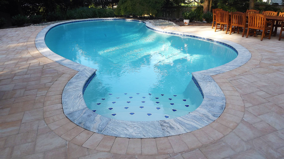 Exempel på en stor klassisk njurformad pool på baksidan av huset, med marksten i betong