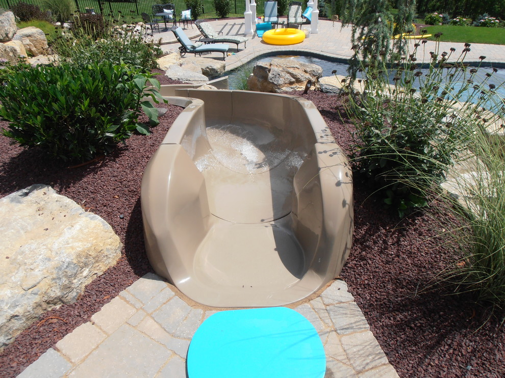 Foto di una piscina naturale chic personalizzata dietro casa con un acquascivolo e pavimentazioni in mattoni