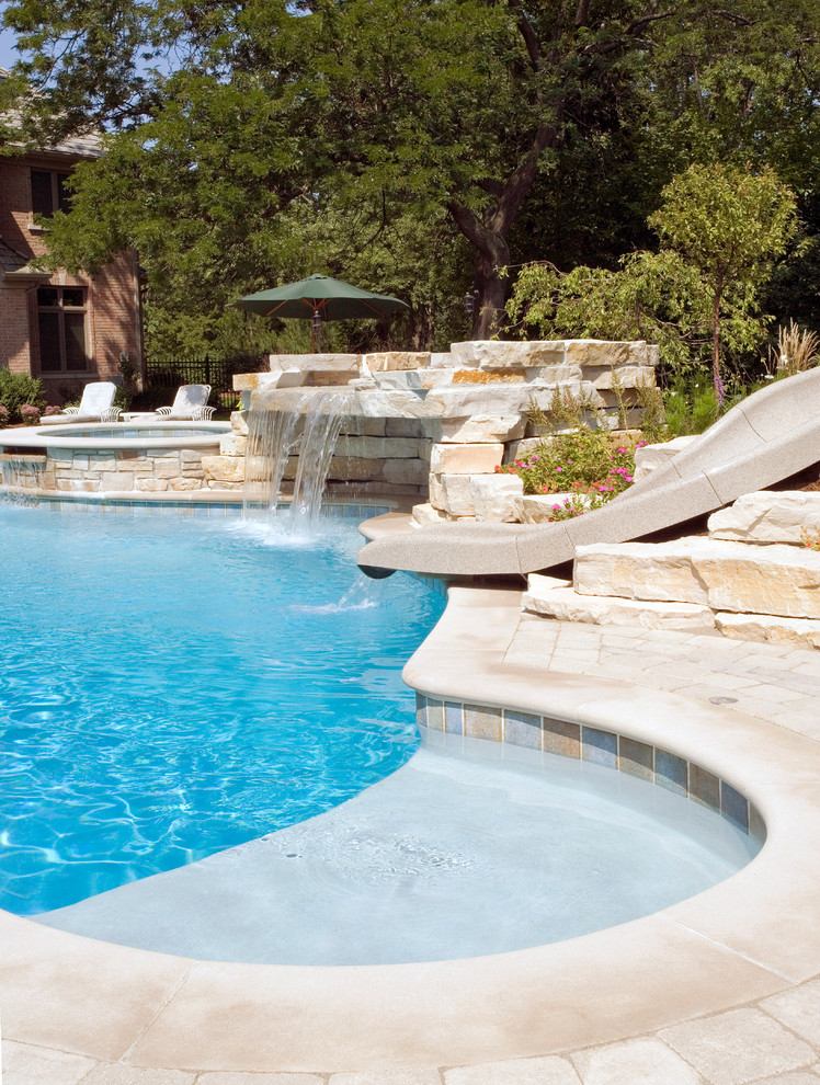 This is an example of an expansive rustic back custom shaped natural swimming pool in Chicago with a water slide and concrete paving.