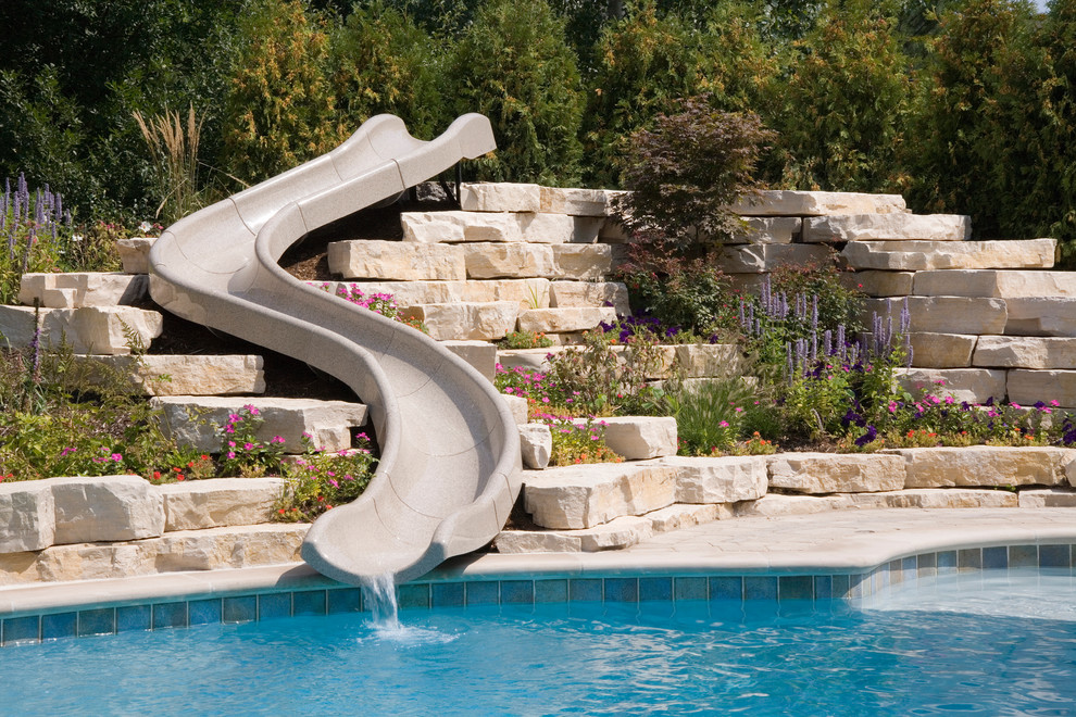 Photo of an expansive rustic back custom shaped natural swimming pool in Chicago with a water slide and concrete paving.