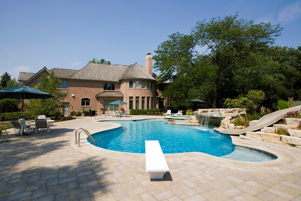 Diseño de piscina con tobogán natural rústica extra grande a medida en patio trasero con adoquines de hormigón