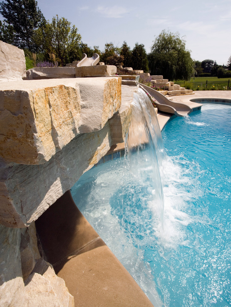Пример оригинального дизайна: огромный естественный бассейн произвольной формы на заднем дворе в стиле рустика с водной горкой и мощением тротуарной плиткой