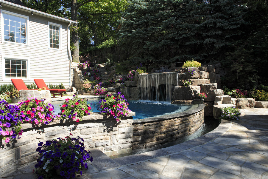 Medium sized classic back custom shaped natural swimming pool in Toronto with a water feature and natural stone paving.