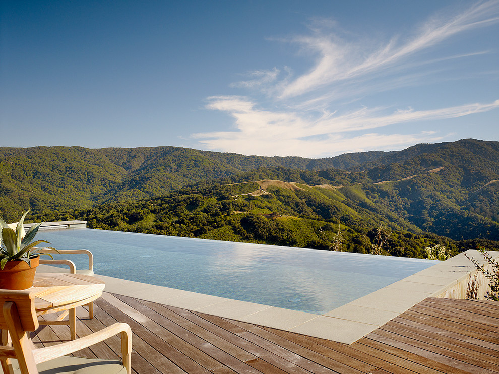 Cette photo montre une piscine à débordement tendance avec une terrasse en bois.