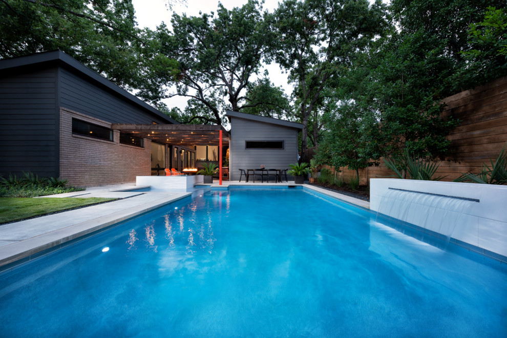 Foto de piscina con fuente moderna de tamaño medio en forma de L en patio trasero con losas de hormigón