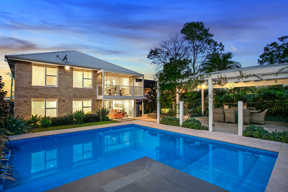 Modelo de casa de la piscina y piscina alargada actual de tamaño medio en forma de L en patio trasero con adoquines de piedra natural