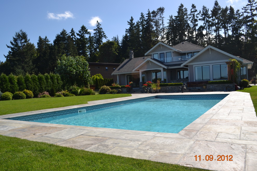 Aménagement d'une grande piscine arrière classique rectangle avec un bain bouillonnant et des pavés en pierre naturelle.