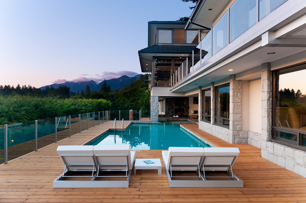 Réalisation d'une grande piscine arrière design sur mesure avec une terrasse en bois.