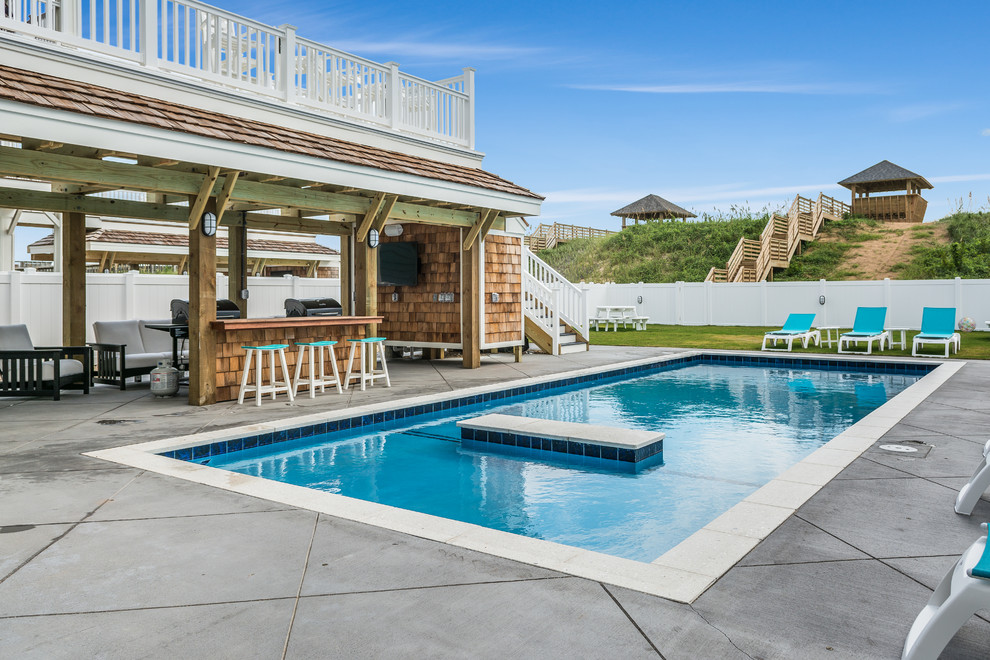 Imagen de piscina costera rectangular en patio trasero con losas de hormigón