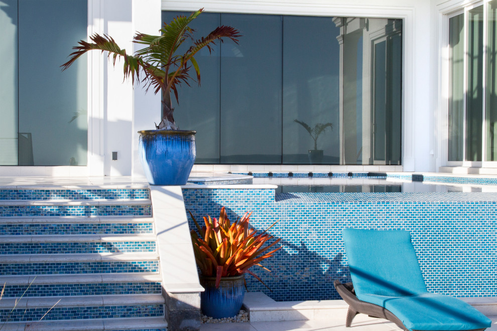 Ejemplo de piscina infinita moderna a medida en patio trasero con adoquines de piedra natural