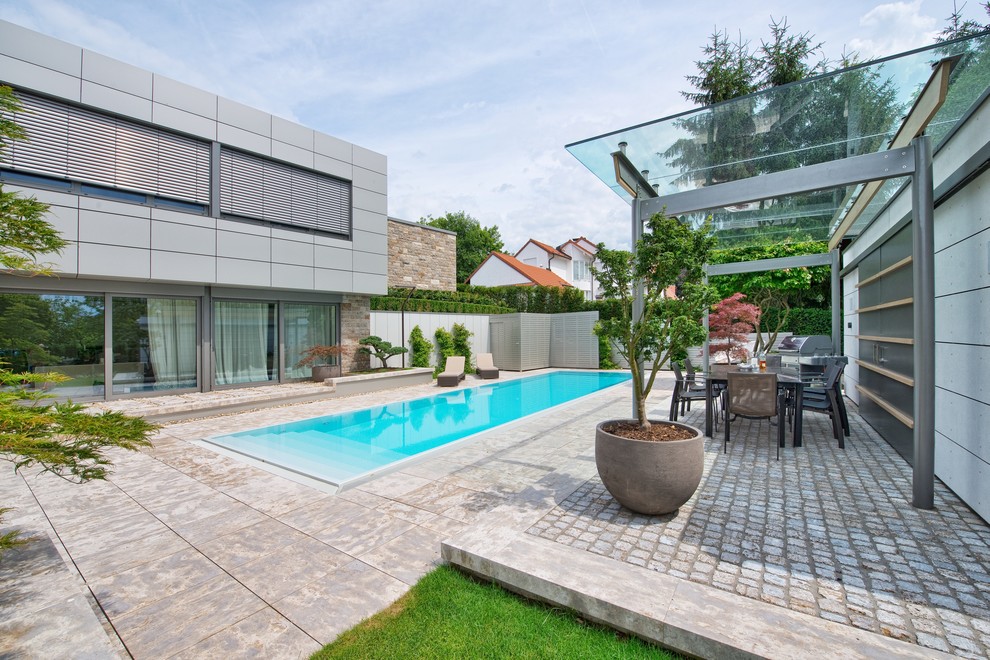 Ejemplo de piscina elevada moderna grande rectangular en patio trasero con adoquines de piedra natural