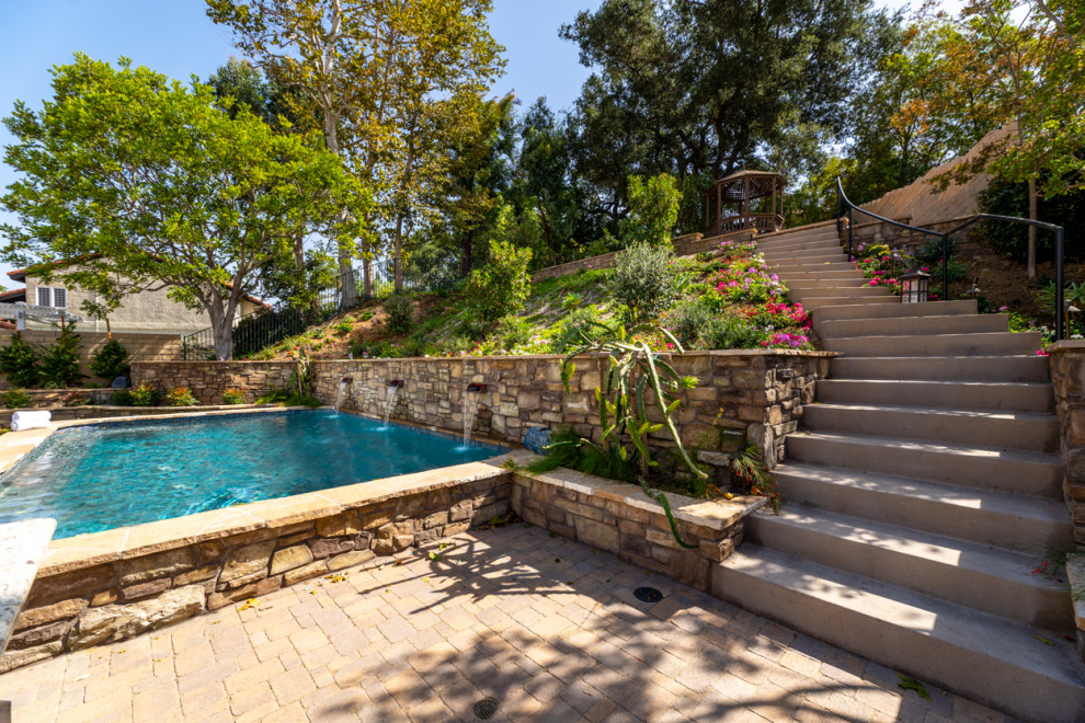 Ejemplo de piscina elevada mediterránea extra grande rectangular en patio trasero con adoquines de piedra natural