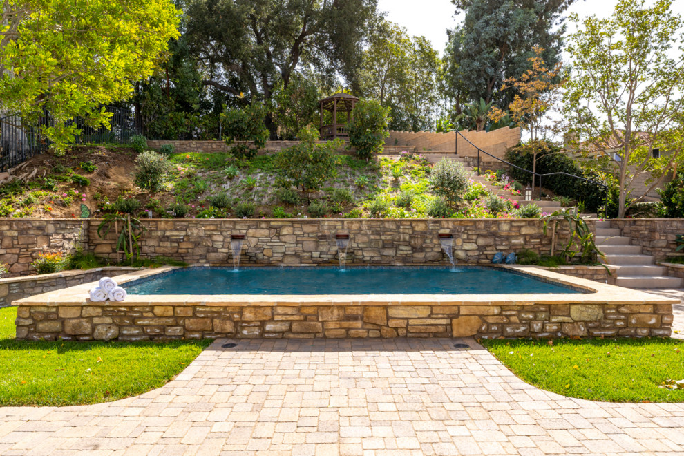 Foto de piscina elevada mediterránea extra grande rectangular en patio trasero con adoquines de piedra natural