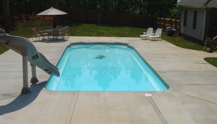 Foto de piscina con tobogán alargada clásica grande rectangular en patio trasero con losas de hormigón