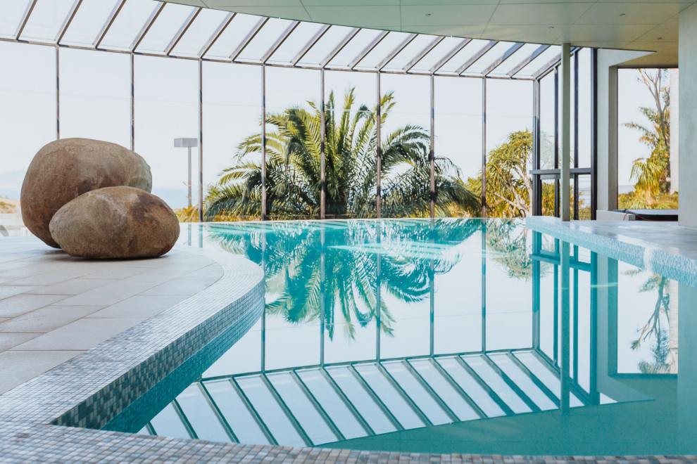 Идея дизайна: большой бассейн-инфинити произвольной формы в доме в современном стиле с перегородкой для приватности и покрытием из плитки