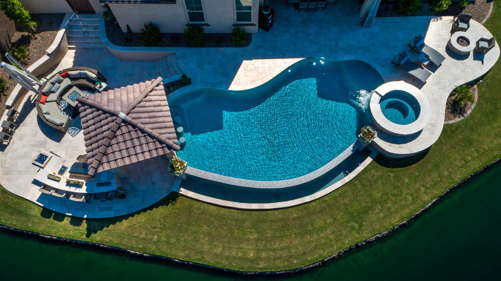 Cette photo montre une piscine à débordement et arrière tendance en forme de haricot de taille moyenne avec un bain bouillonnant et du carrelage.