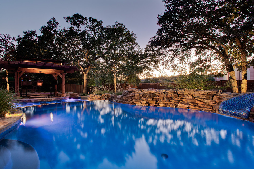 Esempio di un'ampia piscina naturale tropicale personalizzata dietro casa con un acquascivolo e pavimentazioni in pietra naturale