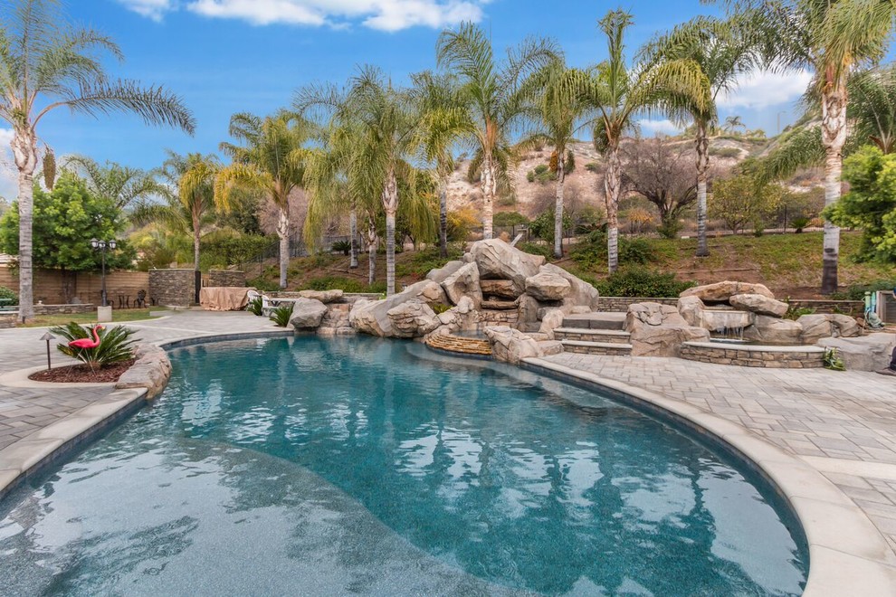 Large island style backyard concrete paver and custom-shaped water slide photo in Orange County