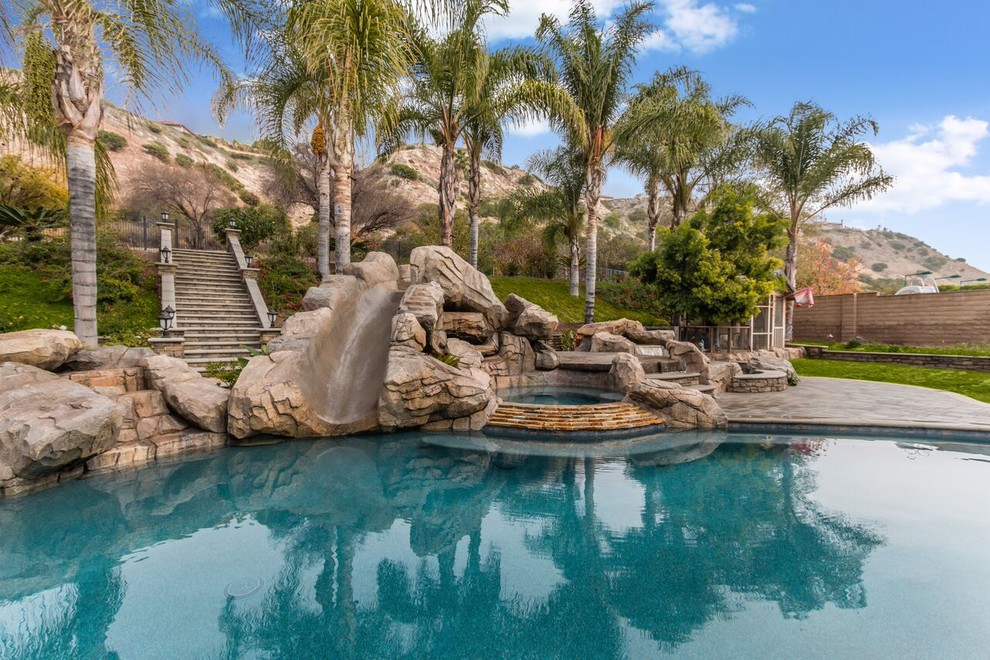 Bild på en stor tropisk anpassad pool på baksidan av huset, med vattenrutschkana och marksten i betong