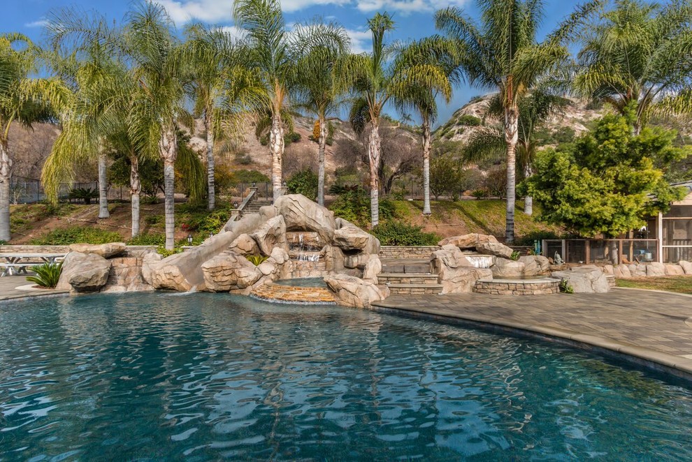 Imagen de piscina con tobogán clásica renovada grande a medida en patio trasero con adoquines de hormigón
