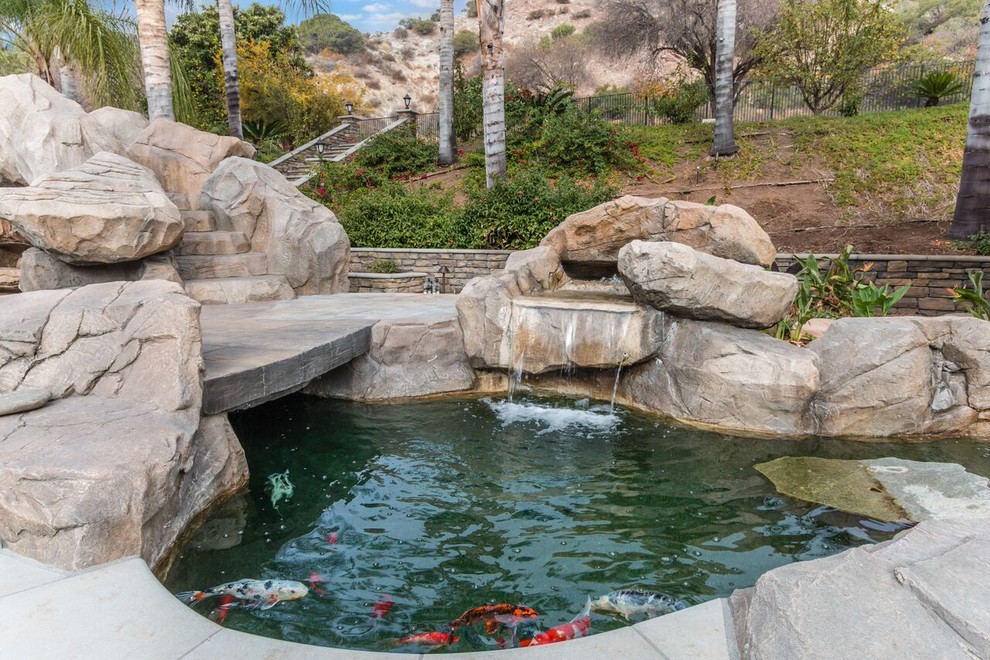 Example of a large island style backyard concrete paver and custom-shaped water slide design in Orange County