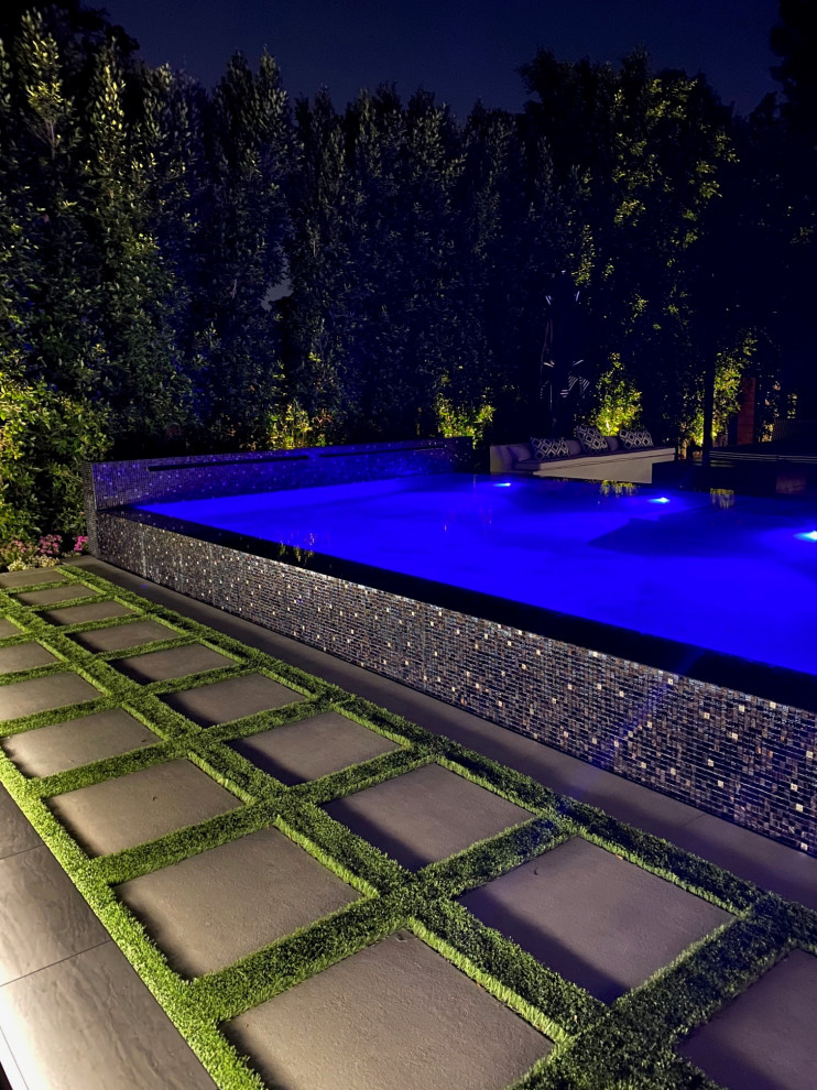 Diseño de piscina infinita minimalista grande rectangular en patio trasero con paisajismo de piscina y suelo de baldosas