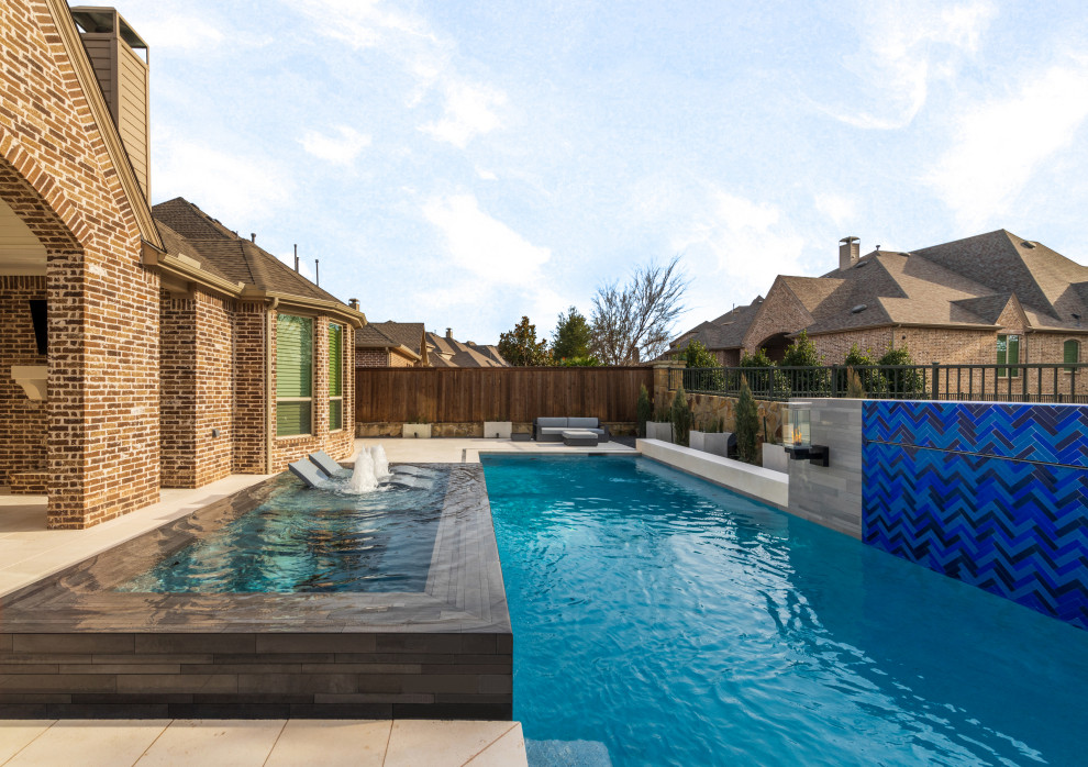 Cette image montre une grande piscine arrière design rectangle avec un bain bouillonnant et des pavés en pierre naturelle.