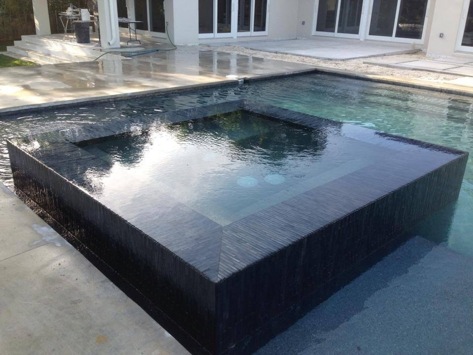 Immagine di una grande piscina a sfioro infinito minimalista rettangolare dietro casa con una vasca idromassaggio e lastre di cemento