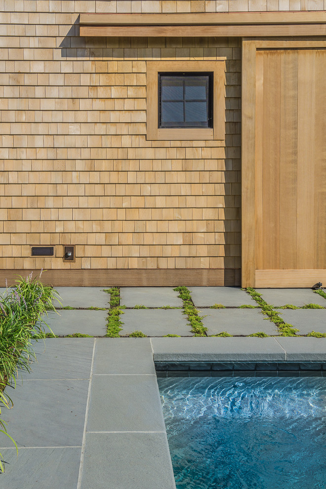 This is an example of a large country back rectangular natural swimming pool in Boston with a pool house and natural stone paving.