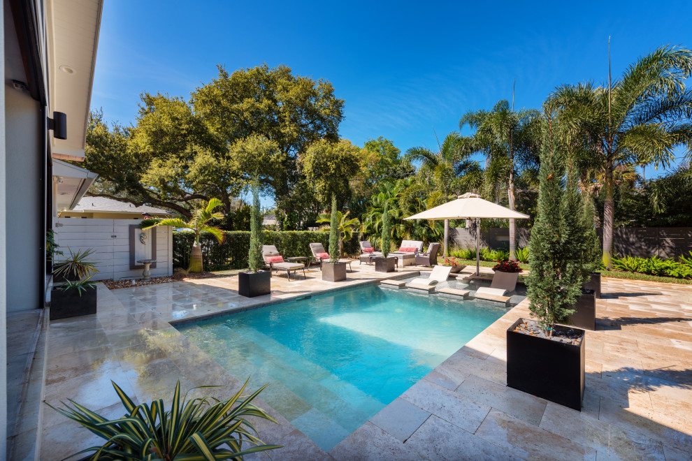 Modelo de piscina clásica de tamaño medio rectangular en patio trasero con adoquines de piedra natural