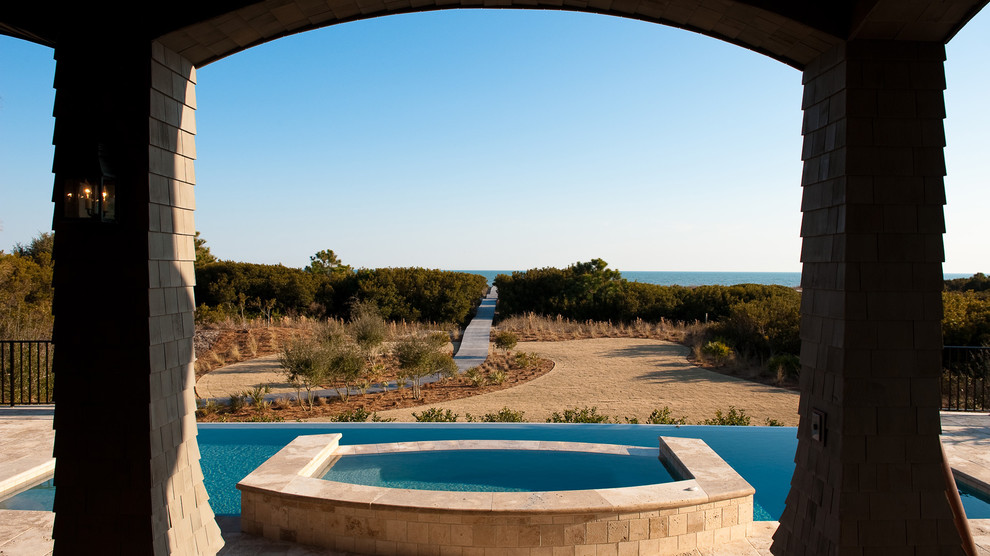 Diseño de piscina infinita tradicional grande rectangular en patio trasero con adoquines de piedra natural