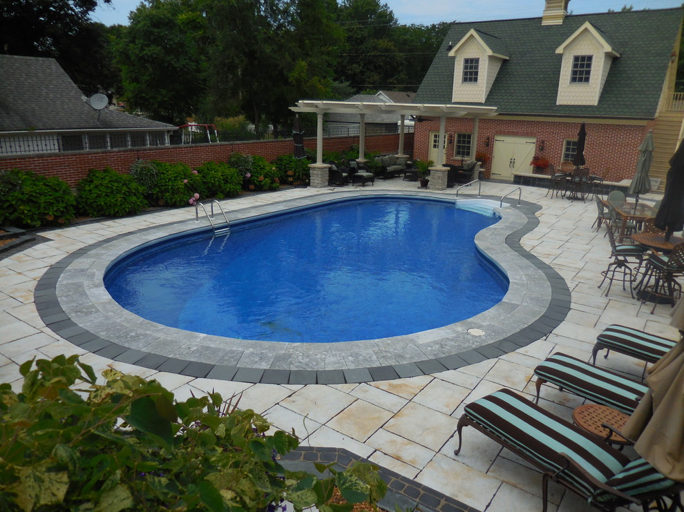 Modelo de casa de la piscina y piscina alargada clásica de tamaño medio tipo riñón en patio trasero con suelo de hormigón estampado