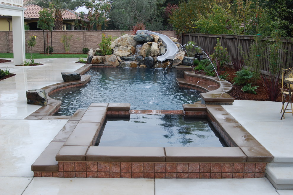 Imagen de piscina con tobogán alargada contemporánea grande a medida en patio trasero con losas de hormigón