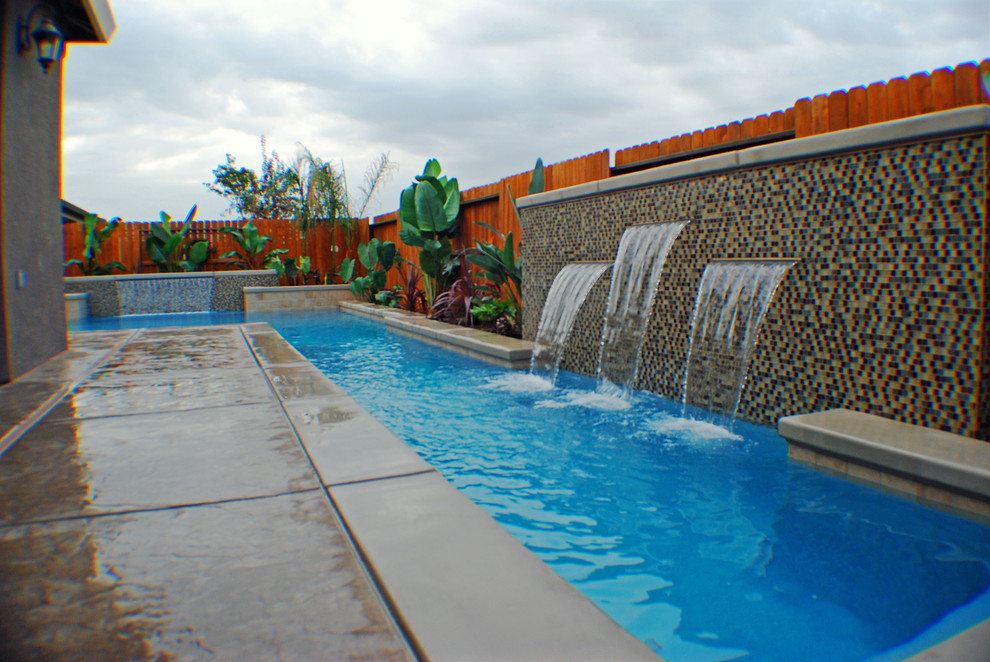 Esempio di una piscina monocorsia contemporanea rettangolare di medie dimensioni e dietro casa con fontane e lastre di cemento
