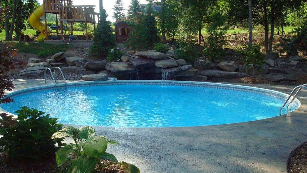 Foto de piscina con fuente clásica de tamaño medio redondeada en patio trasero con adoquines de hormigón