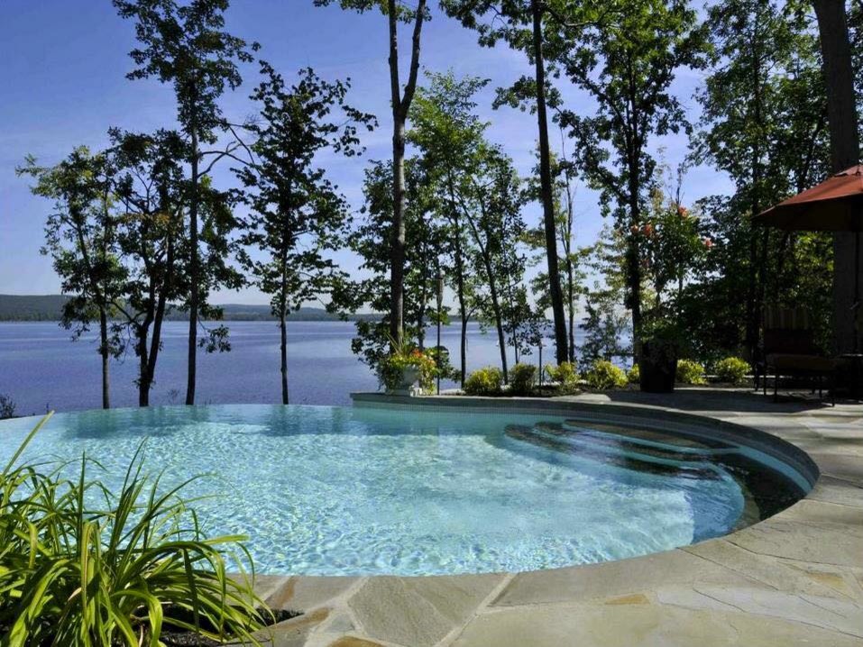 Mittelgroßer Klassischer Infinity-Pool hinter dem Haus in runder Form mit Natursteinplatten in New York