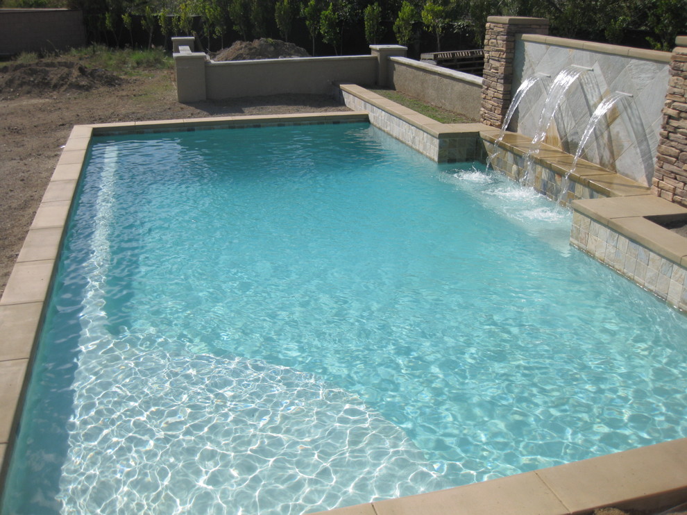 Diseño de piscina con fuente alargada actual de tamaño medio a medida en patio trasero con suelo de hormigón estampado