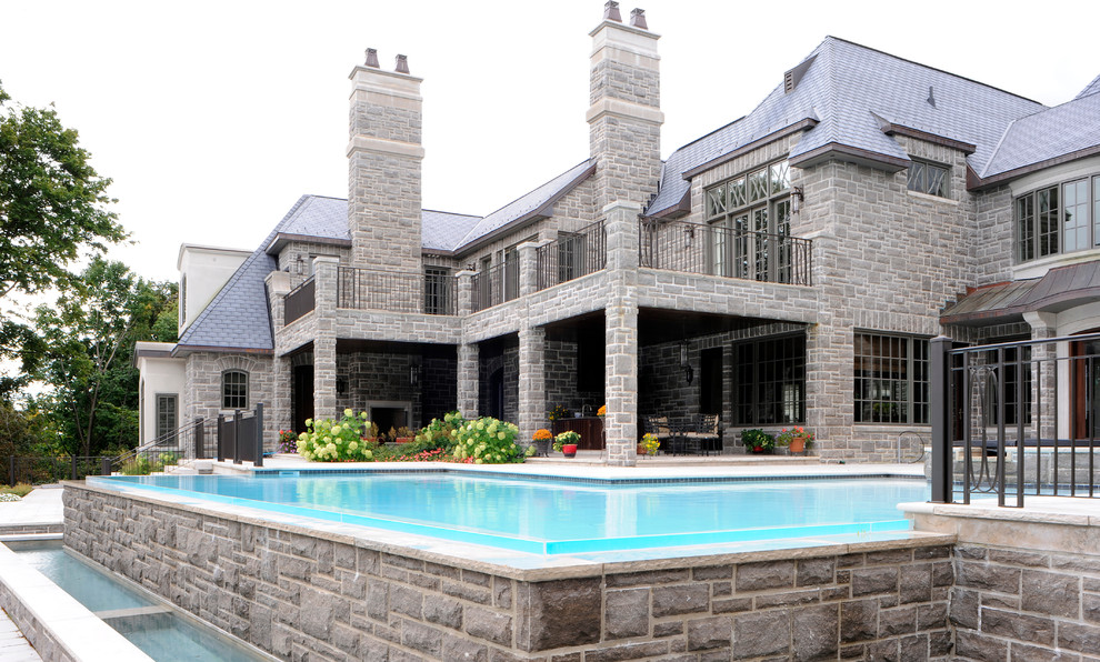 Immagine di una grande piscina a sfioro infinito tradizionale personalizzata dietro casa con pavimentazioni in pietra naturale