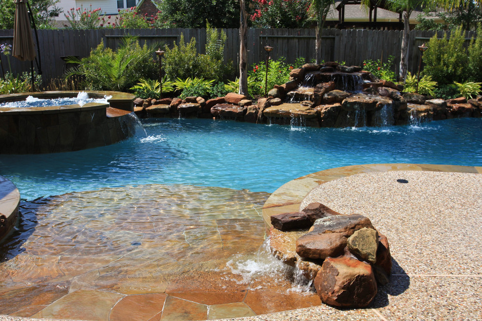 Foto di una grande piscina monocorsia tradizionale personalizzata dietro casa con una vasca idromassaggio e pavimentazioni in pietra naturale
