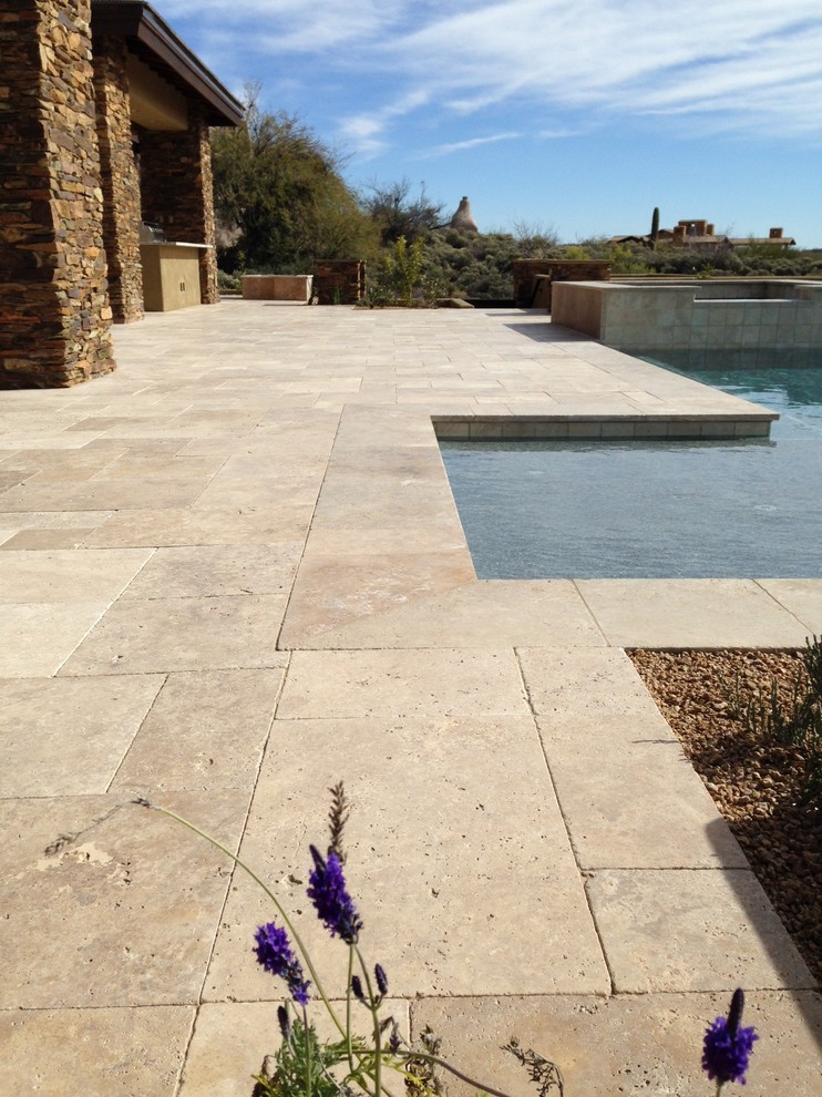 This is an example of a large back l-shaped hot tub in Phoenix with natural stone paving.