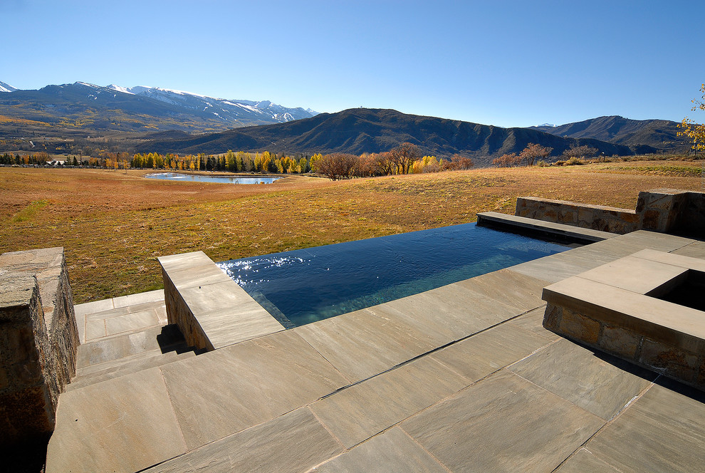 Photo of a large rustic back rectangular infinity hot tub in Denver with natural stone paving.