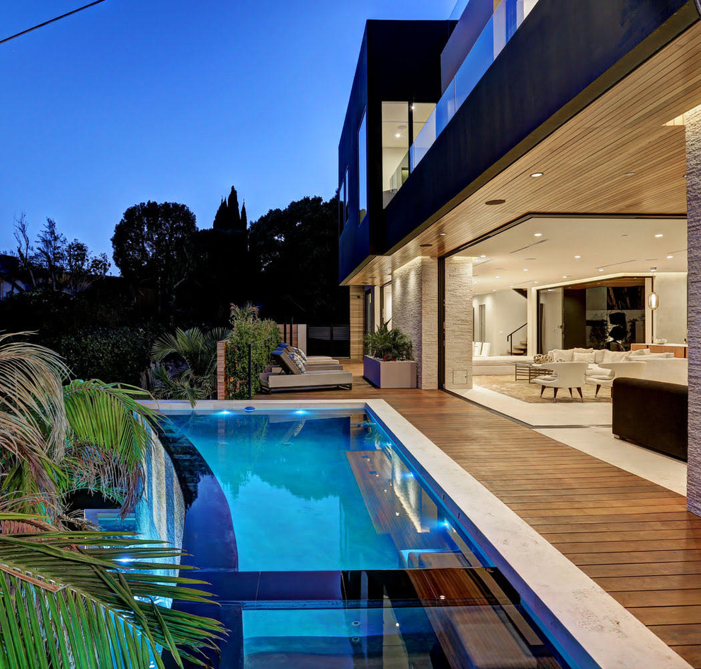 This is an example of a large modern back custom shaped infinity swimming pool in Los Angeles with decking.