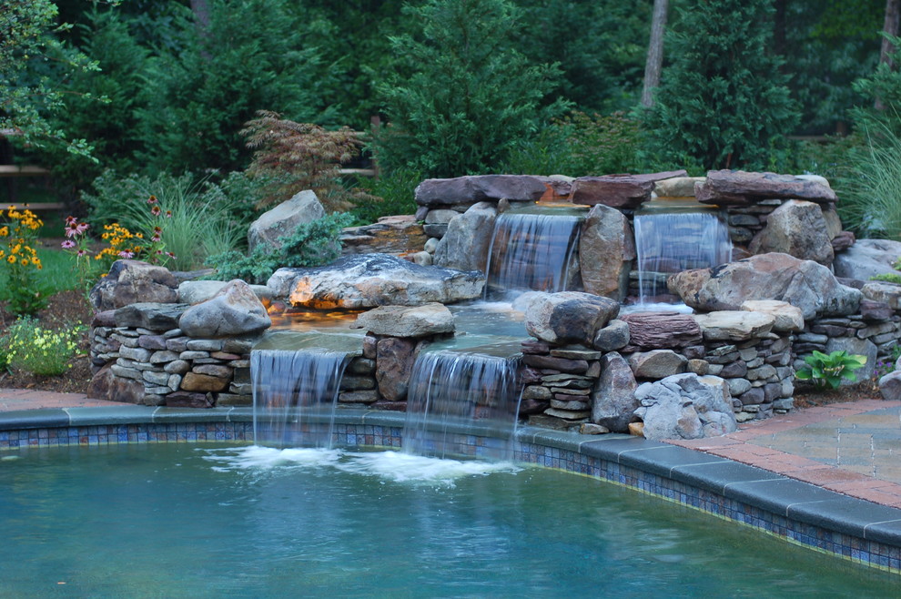 Immagine di una piscina naturale chic personalizzata di medie dimensioni e dietro casa con fontane e pavimentazioni in mattoni