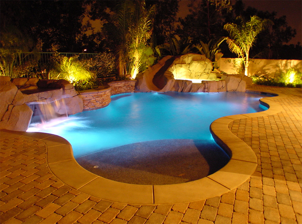 Diseño de piscina con tobogán de tamaño medio tipo riñón en patio trasero con adoquines de ladrillo