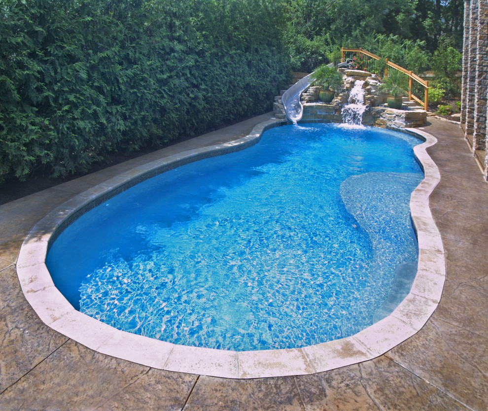 Ejemplo de piscina con tobogán actual de tamaño medio a medida en patio trasero con adoquines de piedra natural