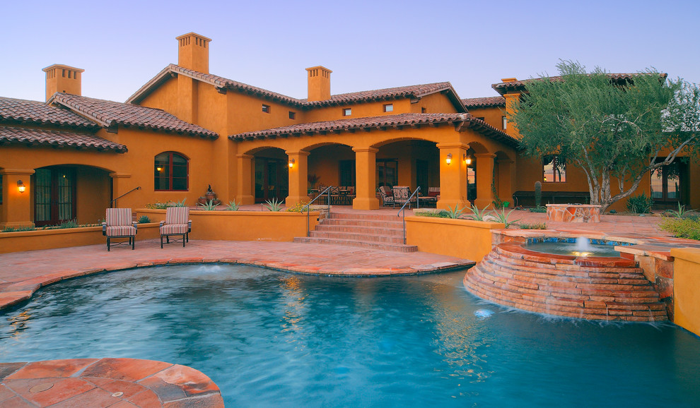This is an example of a large back custom shaped natural swimming pool in Phoenix with a water feature and natural stone paving.