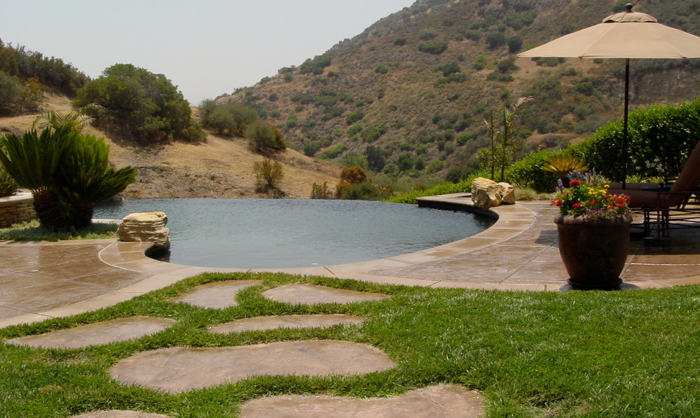 Esempio di una piscina a sfioro infinito classica a "C" di medie dimensioni e dietro casa con una vasca idromassaggio e cemento stampato