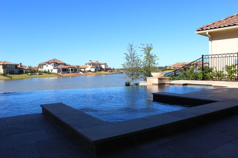 This is an example of a medium sized contemporary back custom shaped infinity swimming pool in Houston with natural stone paving.
