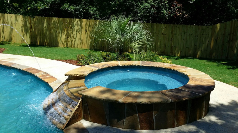 Esempio di una piscina naturale tropicale rotonda di medie dimensioni e dietro casa con una vasca idromassaggio e pavimentazioni in pietra naturale